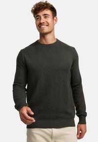 Dunkelolivgrüner gestrickter Pullover mit einem strukturierten Fischgrätenmuster, Rundhalsausschnitt sowie gerippten Bündchen und Saum. Enganliegende Silhouette.