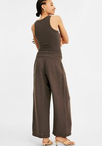 Bruine geribbelde tanktop gecombineerd met losse bruine broek met een gesmockte tailleband. De outfit heeft een zachte, gestructureerde uitstraling.