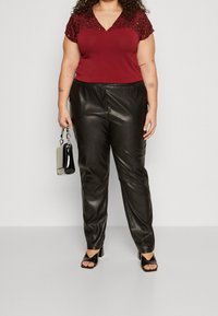 Top burdeos con hombros adornados con lentejuelas, combinado con pantalones de piel sintética negros. La modelo sostiene un pequeño bolso negro y lleva sandalias de tacón alto.