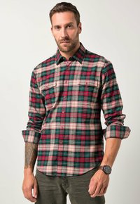 Röd, grön och krämfärgad rutigt flanellskjorta med l�ånga ärmar, knäppt krage och två bröstfickor. Modell med en mörk klocka.
