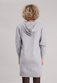 Robe sweat à capuche grise avec des manches longues, un ourlet côtelé et une texture douce. Semble être à longueur de genoux, conçue pour un usage décontracté.