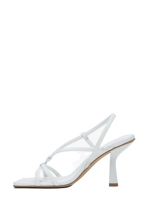 White high-heeled sandal with thin straps, square toe, and a block heel. Smooth texture with a minimalist design and neutral color.