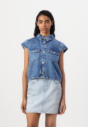 Chemise sans manches en denim avec col, deux poches avant, fermeture à boutons. Associée à une jupe en denim bleu clair avec des motifs à pois.