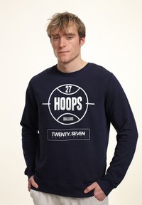 Marinblå sweatshirt i bomull med en stor vit basketgrafik som har texten "HOOPS" och "TWENTY.SEVEN". Ribbad halsringning och muddar.