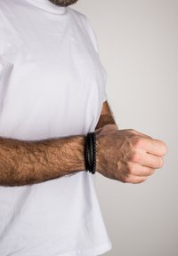 Black leather and bead bracelet worn on a wrist. Bracelet features smooth leather and round beads, showing a layered design.