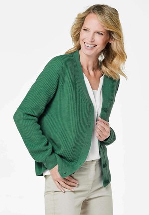 Groene gebreide cardigan met een geribbelde textuur, voorzien van een knoopsluiting aan de voorkant, lange mouwen en een losse pasvorm. Gedragen over een witte top.
