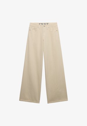 Beige wijd uitlopende spijkerbroek met vijf zakken, riemlussen en een knoopsluiting, weergegeven tegen een witte achtergrond.