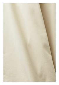 Tessuto di cotone beige con una superficie morbida e testurizzata, che si drappeggia in pieghe delicate. Colore chiaro e neutro con sottili variazioni di tonalità.
