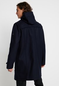 Cappotto in misto lana blu navy con colletto alto e cappuccio. Caratterizzato da maniche aderenti, taglio dritto e dettagli di cucitura sottili sulla schiena.