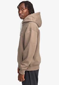 Brown hooded sweatshirt with a loose fit, featuring a drawstring neck, ribbed cuffs, and side seams. Soft texture and casual design.