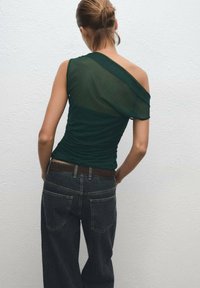 Green, one-shoulder top with ruching, paired with dark denim jeans. The top features a sheer fabric on one side and a solid texture on the other.
