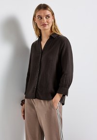 Svart, texturerad skjorta med krage och långa ärmar, i kombination med ljusbruna byxor med sidostripes.