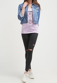 Chaqueta de mezclilla, de manga corta, color azul claro. Camiseta gráfica rosa con corazón y texto. Jeans negros ajustados rasgados. Zapatillas blancas.