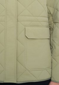 Ανοιχτό πράσινο καπιτονέ μπουφάν με ορθογώνια τσέπη, με ομαλή υφή και οριζόντια ραφή.