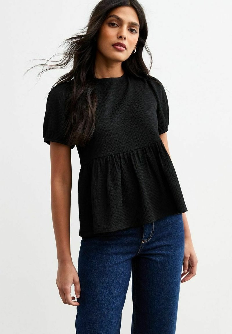 Top nero, strutturato, con scollatura rotonda, maniche corte a sbuffo e orlo peplum. Abbinato a pantaloni in denim blu.
