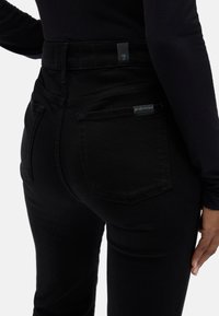Czarne dżinsy z wysokim stanem, o dopasowanym kroju, z tylnymi kieszeniami i metką na pasku. Teksturowana, elastyczna tkanina.