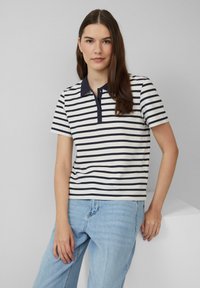 Marineblauwe en witte gestreepte polo met een effen marineblauwe kraag en sluiting. Korte mouwen en een slim-fit ontwerp. Draag het met lichtblauwe jeans.