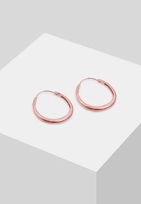 Paire de boucles d'oreilles ovales en or rose brillant avec fermoirs à charnière sécurisés, posées sur une surface blanche inclinée.