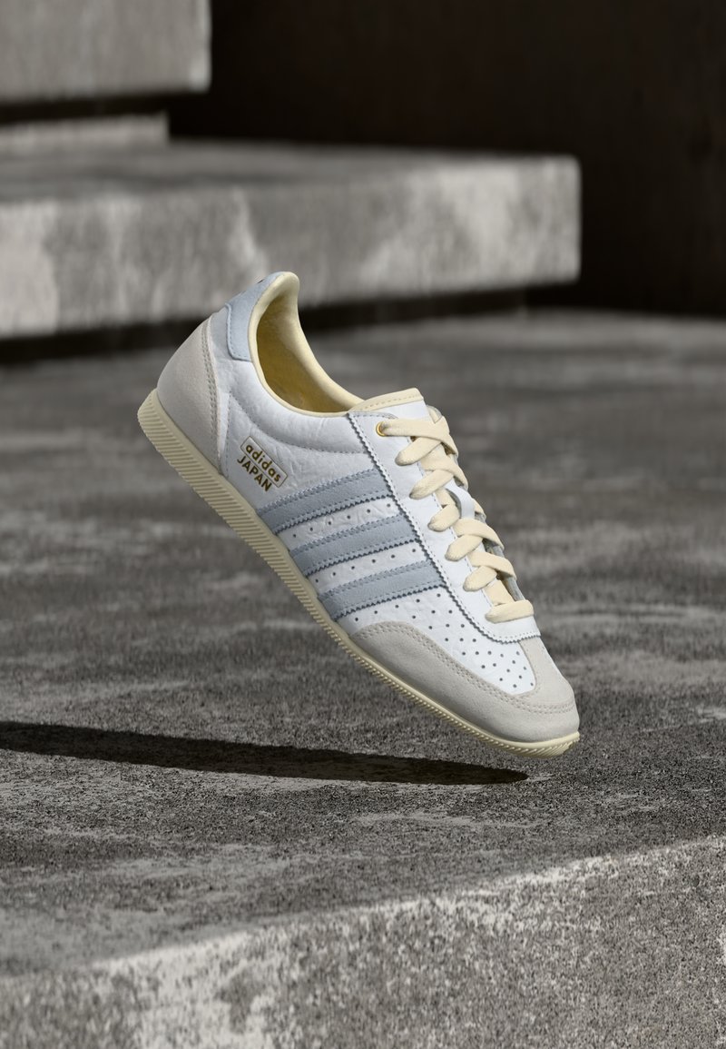 Λευκό και ανοιχτό μπλε αθλητικό παπούτσι με διάτρητα σχέδια, μπεζ κορδόνια και υφασμένο καουτσούκ στη σόλα. Διαθέτει τρεις ρίγες και χρυσό λογότυπο.