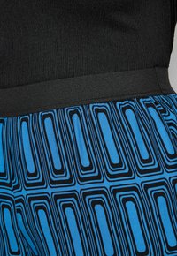 Černý texturovaný top s elastickým pasem, spárovaný s modro-černými kalhotami s geometrickými vzory.