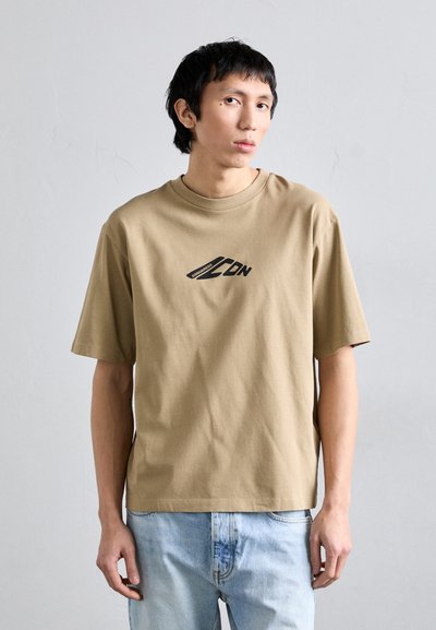 Khaki short-sleeve t-shirt made of cotton, featuring a black graphic logo at the center, with a relaxed fit and crew neckline.