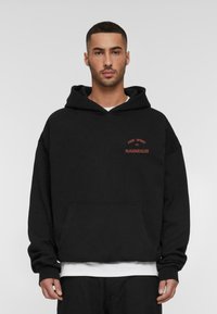 Black cotton hoodie with a front pocket, featuring red embroidered text: "FREE SPIRIT 2004 MJGONZALES." Relaxed fit with a drawstring hood.