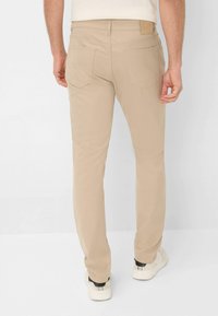 Beige slim-fit broek van een katoenmix, met achterzakken en een leren merkpatch op de taille, gecombineerd met witte sneakers.