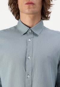 Himmelblaues, knopfbares Hemd aus einem strukturierten Stoff mit einem weichen Finish. Verfügt über einen klassischen Kragen und dezente Logo-Details.