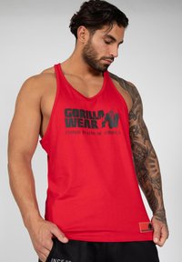 Red tank top made of cotton featuring "GORILLA WEAR" logo in black. Racerback design with a tag on the hem, smooth texture.