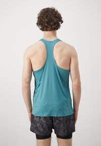 Türkiissinine tank top, millel on võistlusselja disain, valmistatud kergete kangast. Omab tekstuurilise mustriga viimistlust ja on ühendatud mustriliste tumedate lühikestega.