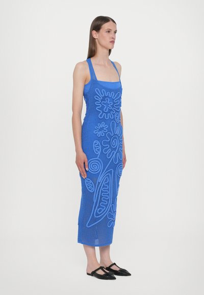 Vestido de punto azul con estampados florales, presenta un escote cuadrado y una silueta ajustada. Modelo llevando zapatos planos negros.