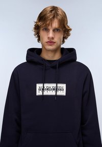 Felpa con cappuccio blu navy, dotata di tasca a marsupio, con una stampa del logo bianco sul petto e cordini sul cappuccio. Tessuto morbido.