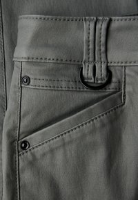 Grått tyg närbild med en texturerad yta, med sömnadsdetaljer, en D-ring ögla och kontrasterande svarta metallaccenter.