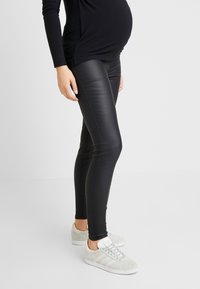 Svarta faux läderleggings med en slank design, som har en åtsittande form och kontrasterande sidostygn, i kombination med ljusgrå sneakers.