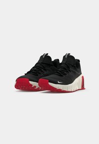 Et par sorte atletiske sneakers med hvide mellemsåler og røde ydersåler, prydet med sorte snørebånd og små hvide og sorte swoosh-logoer.
