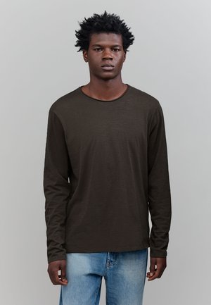 Long-sleeve, dark olive green shirt in a lightweight fabric, featuring a round neckline and relaxed fit. Worn with light blue jeans.