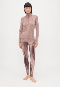 Sobiv sportlik komplekt pehmest, tekstureeritud kangast; ülemisel osal on kõrge krae ja tõmblukk; retuusidel on roosa ja pruuni laineline muster.