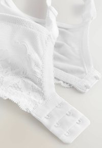 Bralette blanche avec des détails en dentelle florale et en mesh. Bretelles ajustables avec une fermeture à arrière multi-crochets. Tissu doux et texturé sur l'ensemble.