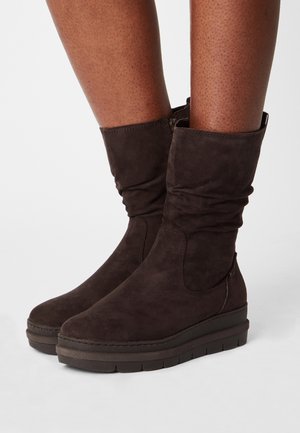 Bottines en daim marron avec un design décontracté, semelle empilée et détail de fermeture éclair latérale. Présentent une texture lisse et un bout arrondi.