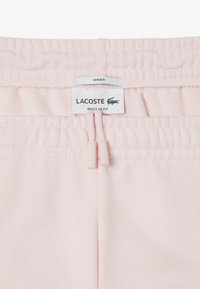 Pantaloni da jogging unisex rosa chiaro con vita regolabile, fascia elastica e etichetta del logo Lacoste. Tessuto morbido, design a vestibilità regolare.