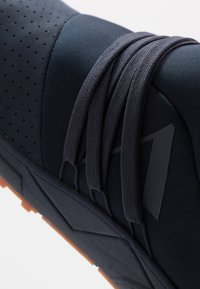 Baskets de sport bleu marine présentant une tige texturée, des perforations, de grosses lacets et une semelle extérieure en caoutchouc avec un motif antidérapant pour plus d'adhérence.
