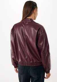 Giacca in pelle sintetica bordeaux con vestibilità rilassata, polsini e orlo a coste, caratterizzata da una texture liscia e un design minimalista.