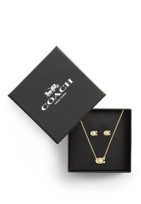 Ensemble de bijoux dorés présenté dans une boîte noire texturée ; comprend un collier chaîne avec une perle et des boucles d'oreilles assorties.
