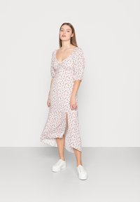 Vestido midi floral em branco, com mangas bufantes, decote profundo, fenda lateral e um tecido leve com padrões florais em rosa e verde.