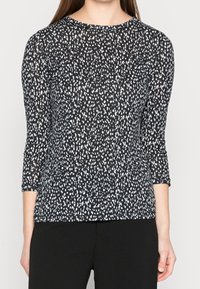 Černý top s třičtvrtinovými rukávy, zdobený bílým tečkovaným vzorem, vyrobený z měkké tkaniny, s kulatým výstřihem a volným střihem.