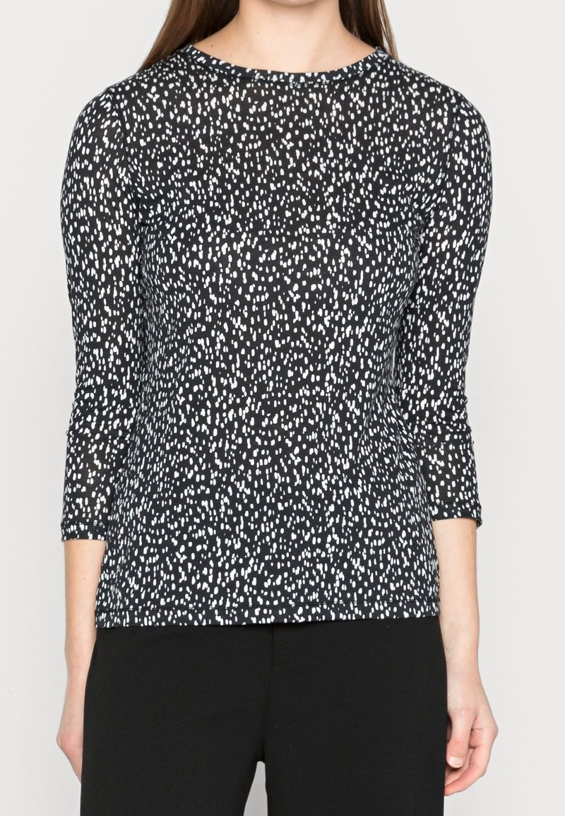 Černý top s třičtvrtinovými rukávy, zdobený bílým tečkovaným vzorem, vyrobený z měkké tkaniny, s kulatým výstřihem a volným střihem.