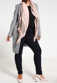 Cappotto grigio in misto lana, top nero, jeans scuri e sciarpa a fantasia rosa chiaro. Tacchi rosa completano l'outfit. Vestibilità standard, design elegante.