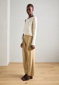 Top cu mânecă lungă cu dungi în nuanțe de crem și bej, asociat cu pantaloni evazați plisati bej și platforme maro cu toc gros. Design minimalist.
