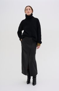 Maglione a collo alto, nero e spesso, abbinato a una lunga gonna aderente in pelle nera con una fessura laterale e una texture liscia. Stivali neri con tacco.