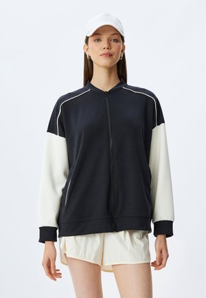 Sort og hvid zip-up sweatshirt med høj krave, ribbede manchetter og kontrasterende ærmedesign. Glat stof med en afslappet pasform.